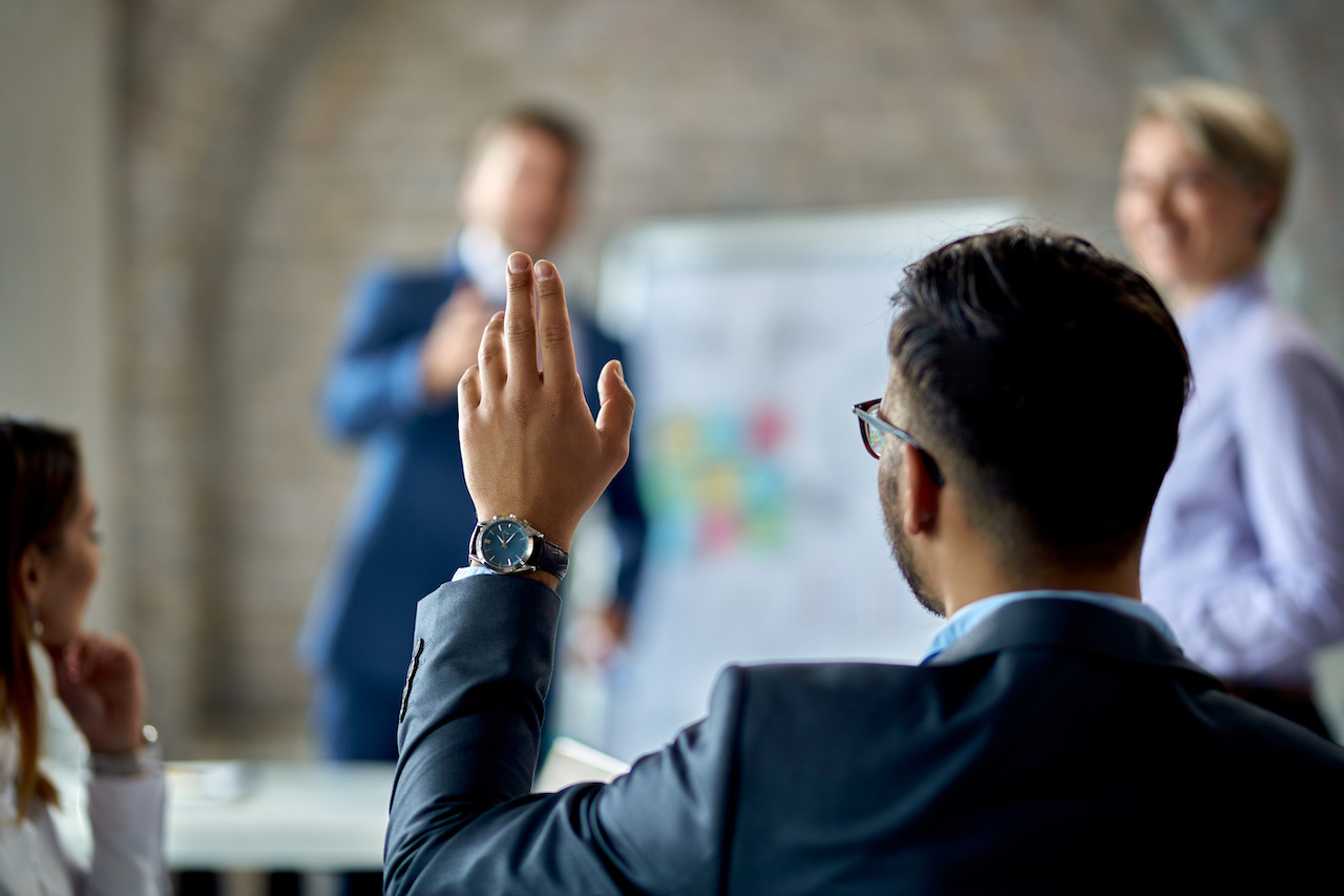 Rear view of a businessman raising his hand to ask the question during business presentation in the office.